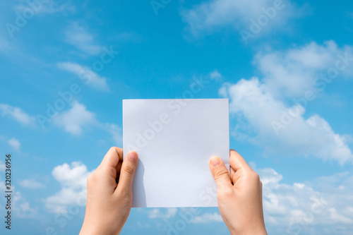 Woman hands holding white paper with blue sky and cloud background. photo