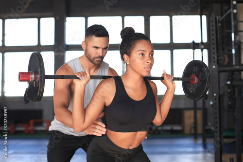 Man and woman with barbell flexing muscles in gym.