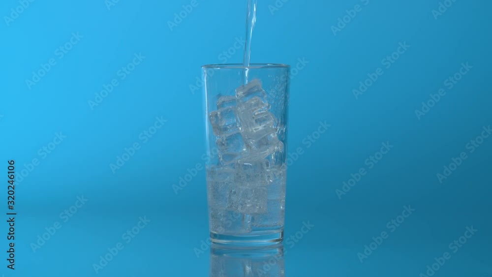 Close up soda, tonic sparkling water pouring into a glass with ice on a blue background. Healthy mineral fizzy water in the glass Close up soda, tonic sparkling water pouring into a glass with ice on a blue background. Healthy mineral fizzy water in the glass