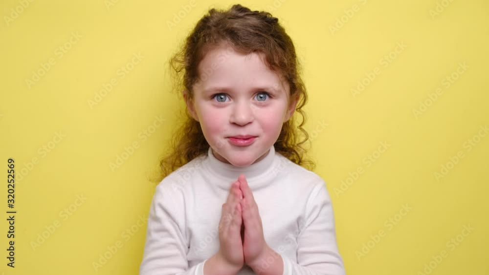 Adorable cute little vlogger looking at webcam, smiling child girl talking to camera making video call vlog communicating online sitting on yellow background. Blogging and people concept