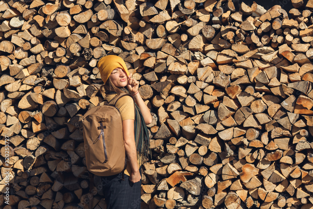 tourist girl posing with backpack on background of stack of firewood. tourist girl posing with backpack on background of stack of firewood.