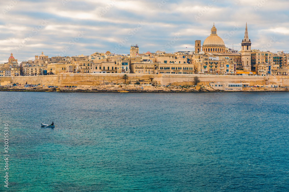 Valletta old town skyline with fisherman in a boat in harbor during sunrise. Malta