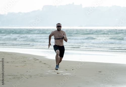 Professional athlete runner man running using heart rate monitor and smart watch training on beach