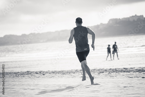 Fitness athlete runner man running barefoot on the beach sand by the sea water