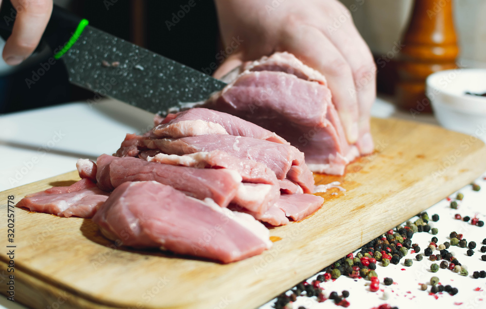 Slicing meat with a knife at home on a kitchen board and pepper