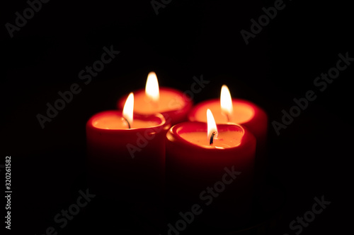 Xmas Christmas season symbol. Four candles symbolize advent weeks. Detail of four red candles burning, isolated with black surrounding.