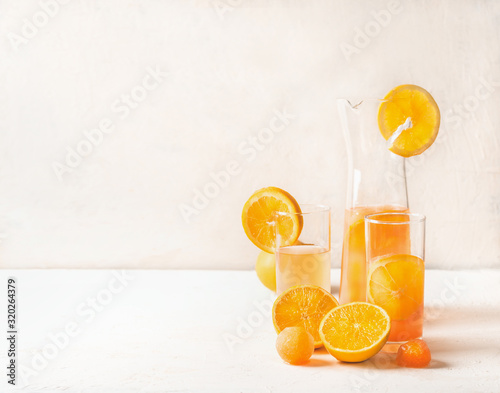 Fototapeta Naklejka Na Ścianę i Meble -  Refreshing orange lemonade with fruits ice cubes of orange juice in jug and glasses on white table