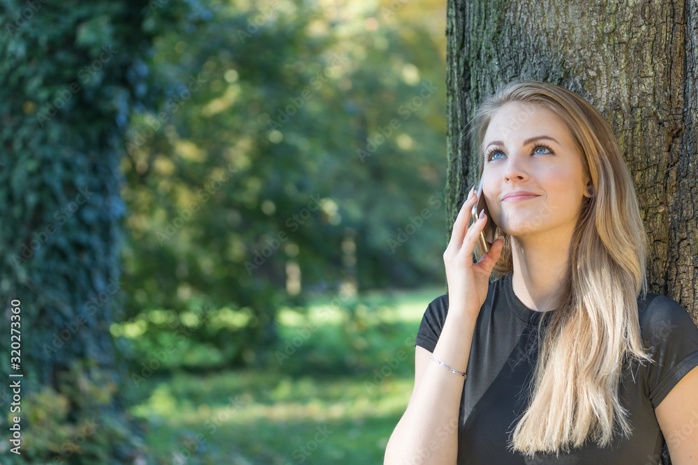 Smiling attractive young girl is phoning in the park. All potential trademarks are removed. Smiling attractive young girl is phoning in the park. All potential trademarks are removed.