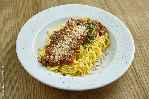 Homemade and fresh pasta bolognese with minced meat, parmesan, tomatoes and basil. Italian pasta spaghetti in white ceramic plate on wooden background. Close up