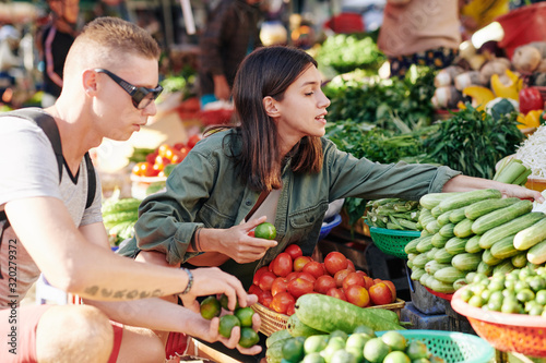 Young couple choosing fresh vegetables at farmer's market, horizontal side view shot