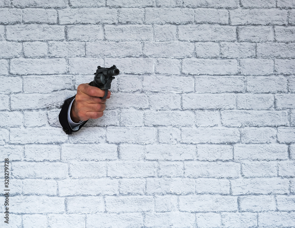 hand with a revolver sticks out of a brick wall