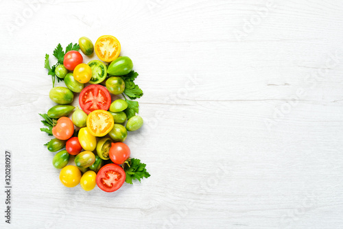 Colored tomatoes and parsley on white wooden background. Fresh vegetables. Top view. Free space for your text.