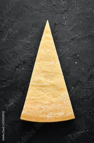 Piece of solid cheese on a black stone background. Parmesan. Top view. Free space for your text.