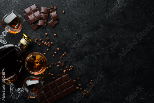 Brandy and chocolate on a black stone table. Top view. Free space for your text.