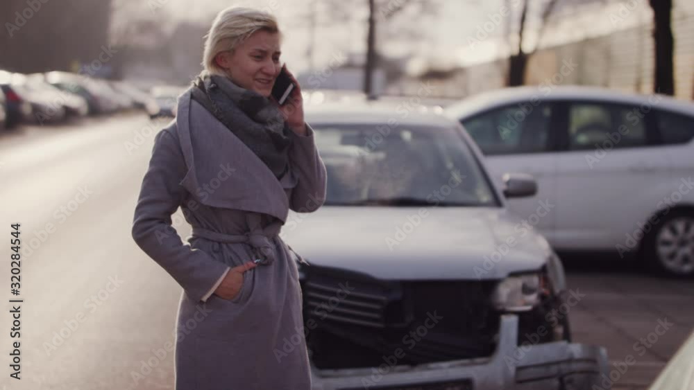 Lonely woman wearing coat standing near car accident scene aside street in a winter day, calling for help on her phone Lonely woman wearing coat standing near car accident scene aside street in a winter day, calling for help on her phone