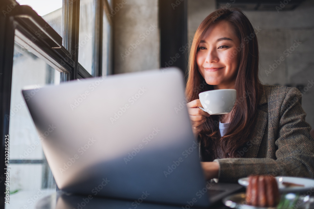 Closeup image of a woman working and typing on laptop computer while drinking coffee in cafe Closeup image of a woman working and typing on laptop computer while drinking coffee in cafe