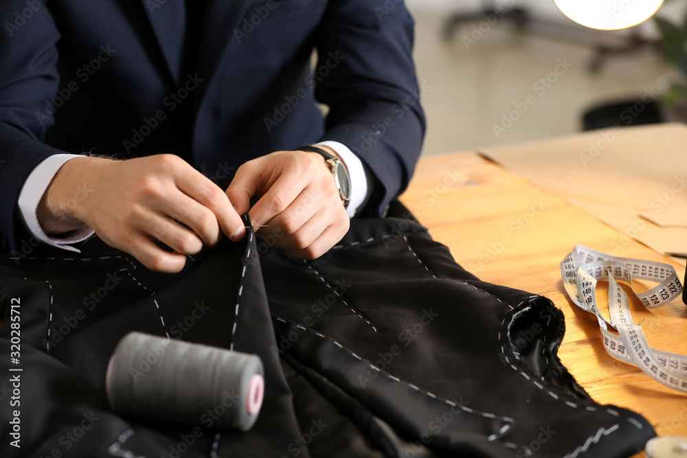 Young tailor working at table in atelier, closeup