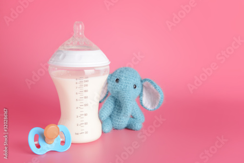 Bottle of milk for baby and toy with pacifier on color background photo