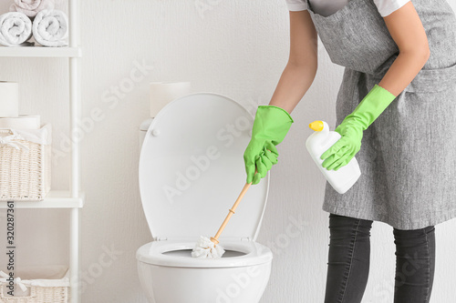 Young woman cleaning toilet in bathroom photo