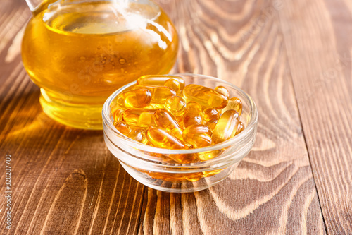 Jug of fish oil and capsules on wooden background