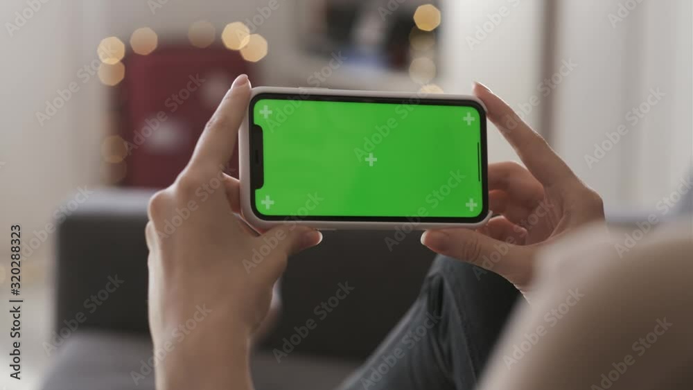 One person use smart phone for browsing social networks and communicating closeup. Young woman at home lying on couch using green screen smartphone in horizontal position. Girl watching video content