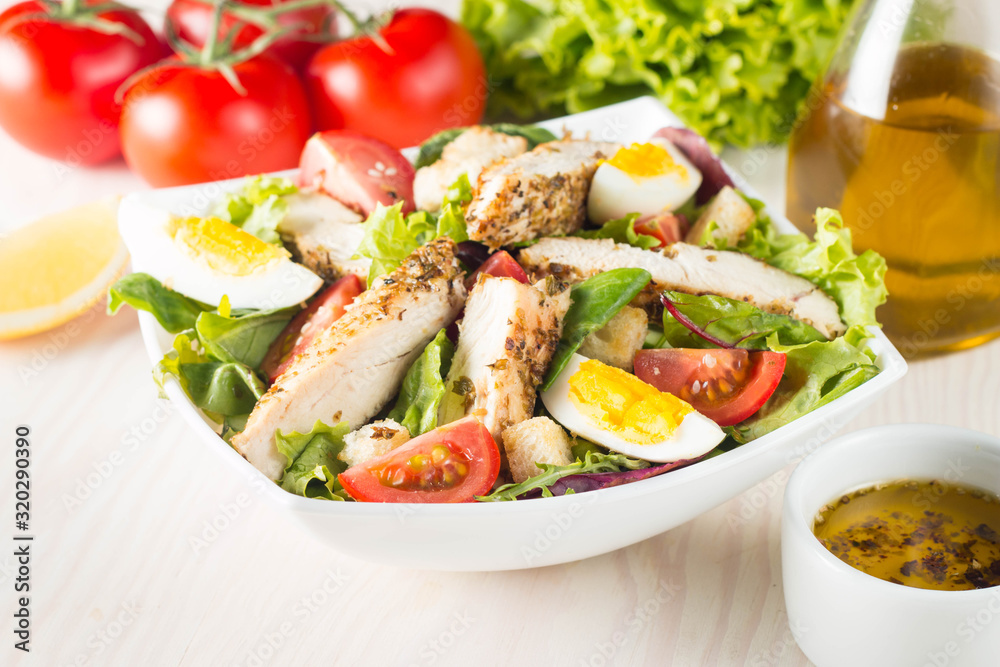 Fresh Caesar salad with delicious chicken breast, ruccola, spinach, cabbage, arugula, egg, parmesan and cherry tomato on wooden background. Oil, salt and pepper. Healthy and diet food concept. Fresh Caesar salad with delicious chicken breast, ruccola, spinach, cabbage, arugula, egg, parmesan and cherry tomato on wooden background. Oil, salt and pepper. Healthy and diet food concept.