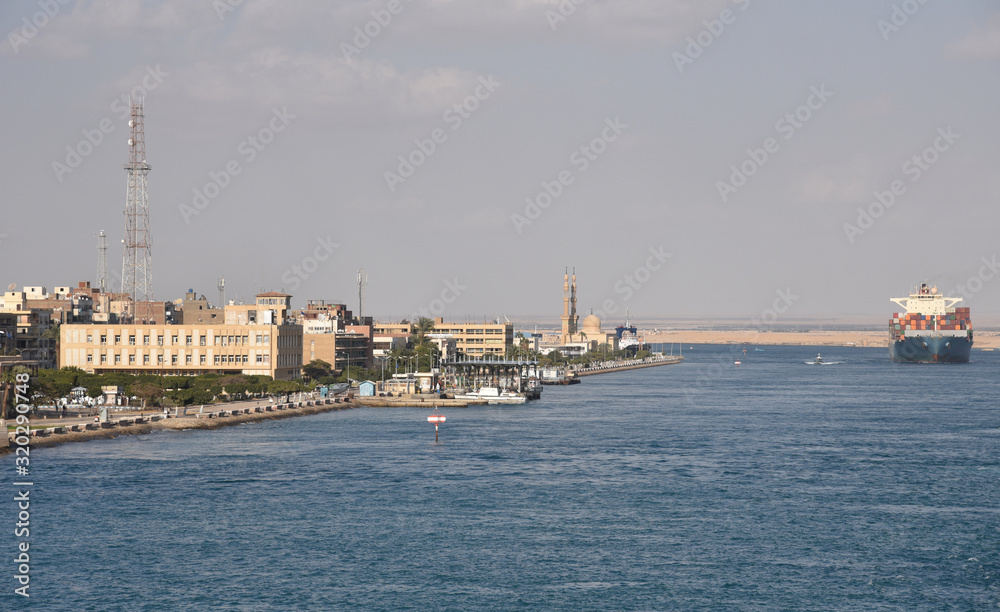 Suez Canal south entrance, view on the city  and transiting cargo ship. 