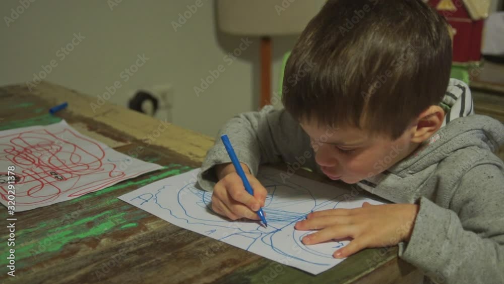 Caucasian toddler boy draws with colour markers on paper and smiles at camera with satisfaction Caucasian toddler boy draws with colour markers on paper and smiles at camera with satisfaction