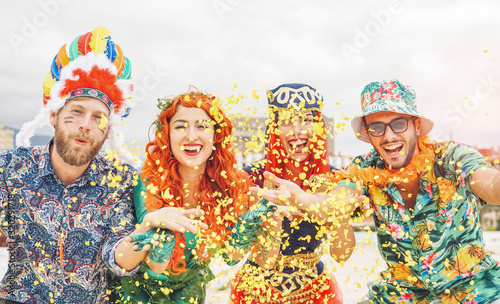 Happy friends celebrating at carnival Brazilian party - Young people wearing carnival costumes having fun throwing confetti and laughing together outdoor - Concept of youth lifestyle holidays
