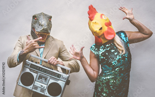 Crazy senior couple wearing chicken and t-rex mask while dancing outdoor - Mature trendy people having fun celebrating and listening music with boombox - Absurd concept of masquerade funny holidays