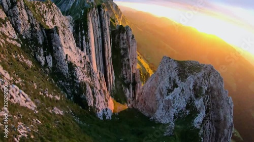 Slow motion, FPV drone shot, passing rocky, mountain peaks, over a man standing on the top of the Appenzell ridge, at sunset, in the alps of Switzerland photo