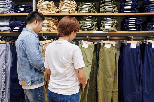 Man and woman looking for good trousers in modern clothes shop, horizontal medium back view shot