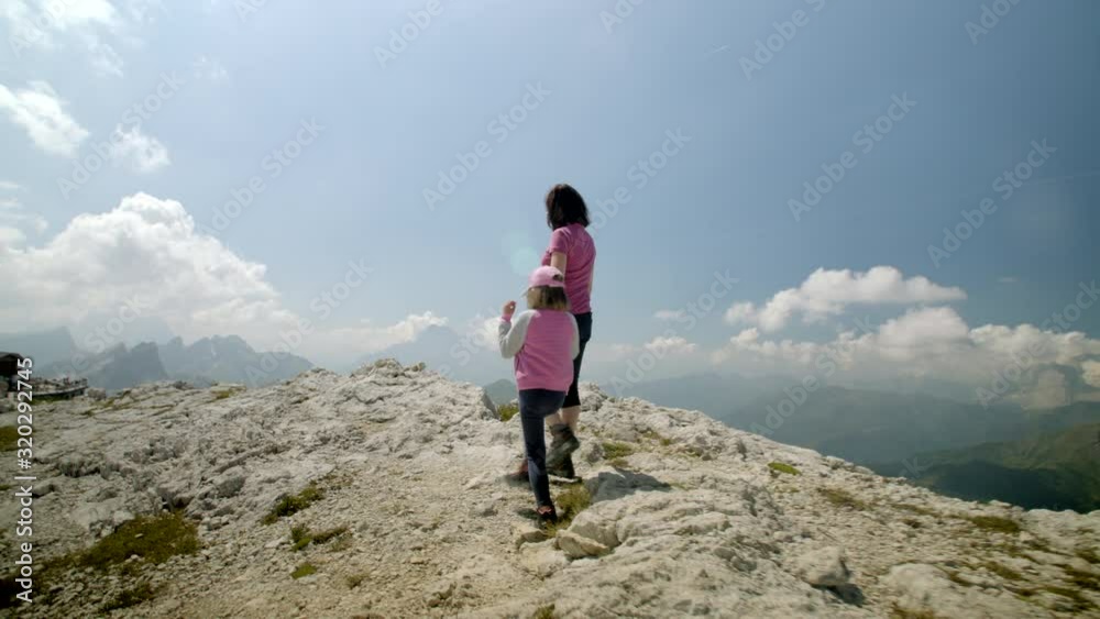 Mother and little daughter hold hands and walk towards mountain edge admiring rocky breathtaking mountains on a sunny summer day, Dolomites, Italy, 4k, prores Mother and little daughter hold hands and walk towards mountain edge admiring rocky breathtaking mountains on a sunny summer day, Dolomites, Italy, 4k, prores