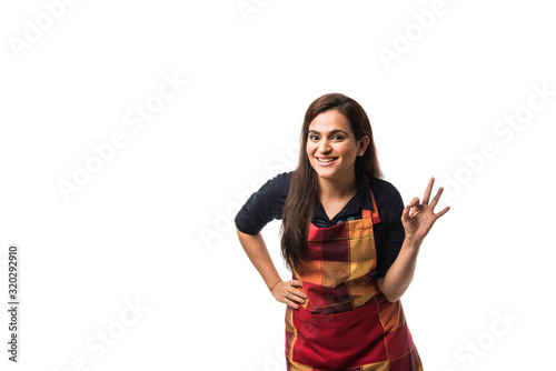 Portrait of Indian woman chef or cook in apron, presenting, pointing, with ok sign, thumbs up or hands folded. standing isolated over white background photo