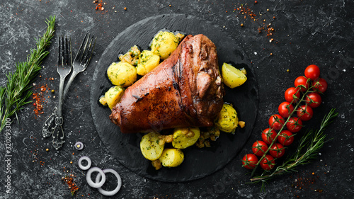 Photography Baked pork leg with potatoes on a black stone plate