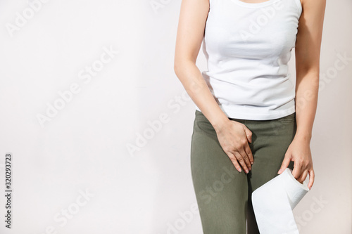 Woman hand holding her crotch lower abdomen and tissue or toilet paper roll.