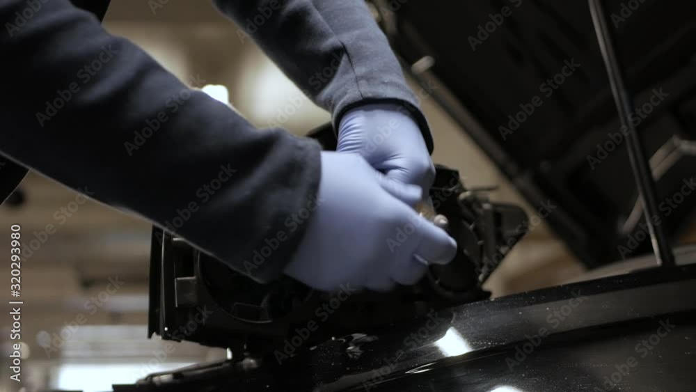 A mechanic changing a broken halogen lamp from a car's headlight. Professional expertise in action.
A mechanic changing a broken halogen lamp from a car's headlight. Professional expertise in action.
