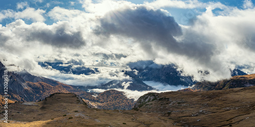 Panoramic view of Dolomite mountains in autumn season with sun shining through the clouds