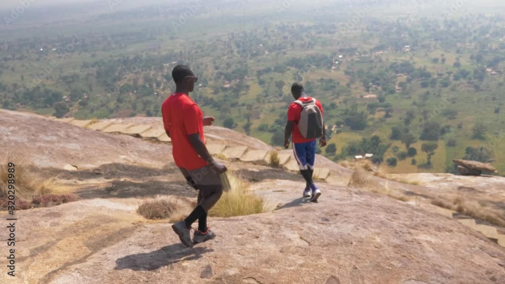 A tracking shot from behind of two African men jogging and walking down a steep granite mountain in Africa. A tracking shot from behind of two African men jogging and walking down a steep granite mountain in Africa.