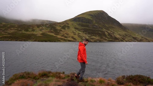 Static shot of a man celebrating and walking at the coast of lake Loch Skeen, on a dark day, in Dumfries and Galloway, Scotland, UK photo