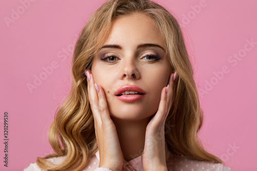 Portrait of beautiful tender curly blonde woman with clean skin posing on pink background.