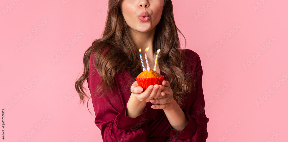 Unrecognizable woman blowing colourful candles on birthday cupcake - obrazy, fototapety, plakaty 