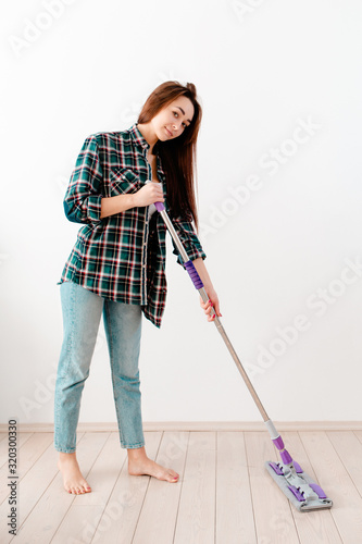 The concept of cleaning. Woman in casual clothes washing floors. There is a white wall in the background. There's a clean cleaning trail on the floor. Copy space
