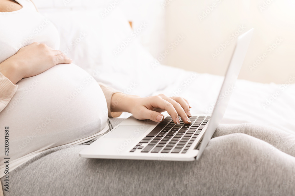 Fototapeta premium Pregnant woman browsing on laptop at home, side view, free space
