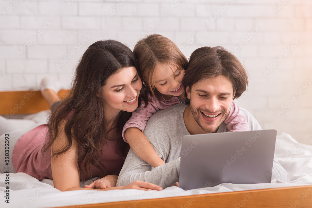 Young Parents And Their Little Daughter Using Laptop In Bed Young Parents And Their Little Daughter Using Laptop In Bed