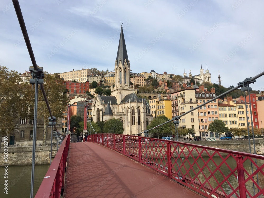 Obraz premium The Saint-Georges Roman Catholic church seen from the Paul Couturier bridge in Lyon, France. In the background the Basilica of Notre-Dame de Fourvière and the Metallic tower of Fourvière