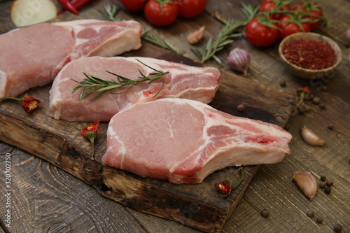 fresh raw pork meat isolated on a wooden cutting board and tomatoes and spices on a rustic wooden background. 