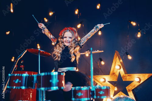 Beautiful girl with curly hair playing the drums on a black illuminated background © zamuruev