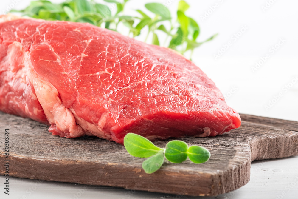 Fototapeta premium Fresh juicy piece of fresh beef with greens on a wooden Board on a white wooden background.