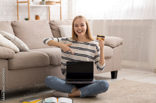 Happy girl holding credit card and pointing at laptop screen photo